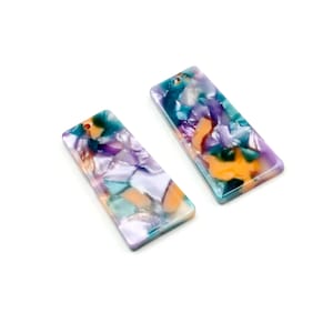 May include: Two rectangular acrylic charms with a marbled pattern in shades of purple, teal, orange, and white. Each charm has a small hole at the top for attaching to jewelry or other crafts.