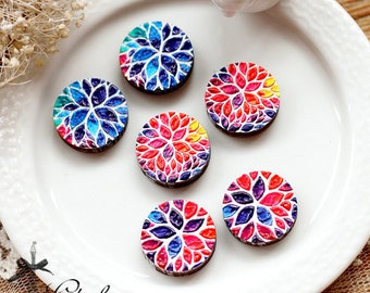 May include: Six round, wooden decorative magnets with colorful floral designs. The magnets feature a variety of colors, including blue, red, and yellow. The magnets are arranged on a white plate. The text "Clothcamp create your own style" is in the bottom left corner.