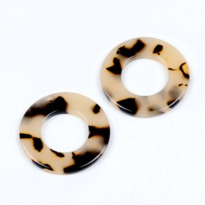 May include: Two round, cream-colored, resin earrings with a black and brown tortoiseshell pattern.