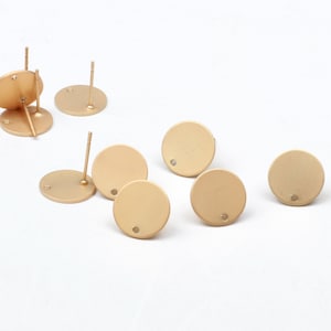 May include: A set of eight gold-toned metal earring blanks. Each blank is a round disc with a small hole in the centre. The blanks are designed for use with earring posts.