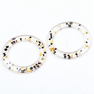 May include: Two clear plastic rings with gold and black glitter embedded inside. The rings are approximately 2 inches in diameter.