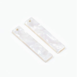 Puede incluir: Dos piezas rectangulares blancas de joyería con un agujero en el centro. La joyería está hecha de un material blanco que se asemeja a la madreperla.