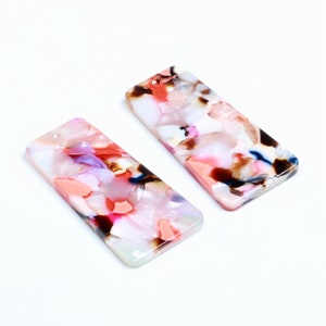 Puede incluir: Dos piezas rectangulares de resina acrílica con un patrón abstracto de colores. Las piezas son blancas con remolinos rosas, rojos, azules y marrones.