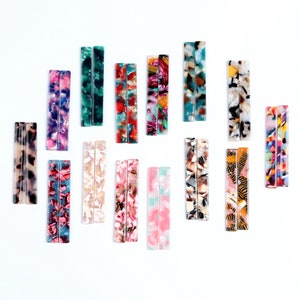 Peut inclure: Assortiment de pinces à cheveux colorées et à motifs. Les pinces sont en plastique et ont une forme rectangulaire. Les motifs comprennent des designs abstraits, des imprimés animaliers et des formes géométriques.