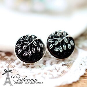 Puede incluir: Un par de pendientes de plata con diseños de árboles en blanco y negro. Los pendientes son redondos y tienen un marco de metal plateado.