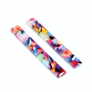 May include: Two rectangular, colorful acrylic earring components. The components are a mix of red, yellow, blue, purple, and green. Each component has a small hole at the top for attaching to earring hardware. The components are approximately 3 inches long.