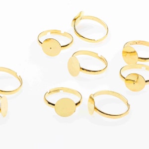 May include: Eight gold-toned adjustable ring blanks with round bezels. The bezels are designed to hold a cabochon or other embellishment.