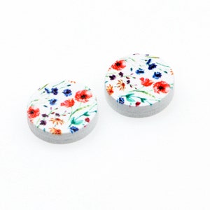 May include: Two round white wooden earrings with a floral print. The print features red, orange, blue, and green wildflowers.
