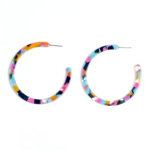May include: A pair of colorful hoop earrings with a marbled pattern in shades of blue, pink, yellow, and black.