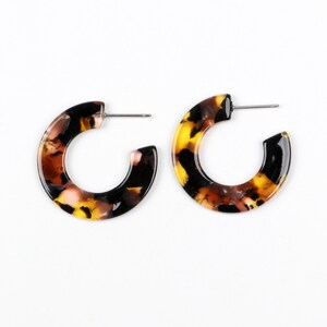 May include: A pair of hoop earrings with a tortoiseshell pattern. The earrings are made of a brown, black, and yellow plastic material.