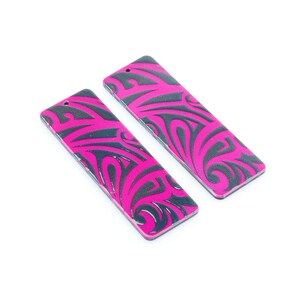 Puede incluir: Dos pendientes rectangulares de color rosa y negro con un patrón tribal.