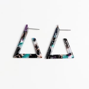 Puede incluir: Un par de pendientes en forma de triángulo con un patrón de mármol negro, blanco, azul y morado.
