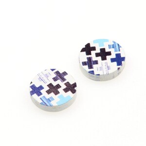 May include: Two round wooden buttons with a white background and a pattern of black and blue crosses.