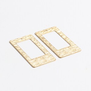 May include: Two gold-toned metal rectangular earrings with a cutout in the center. The earrings have a textured surface.