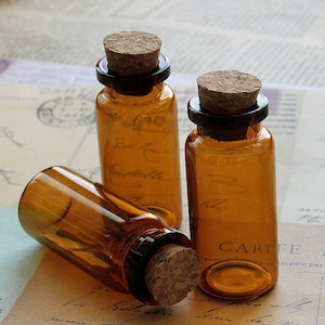 Puede incluir: Tres botellas de vidrio ámbar con tapones de corcho. Las botellas están vacías y tienen un aspecto vintage.