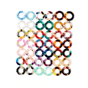 May include: Assortment of colorful, round, plastic rings with a variety of patterns. The rings are arranged in a grid pattern.
