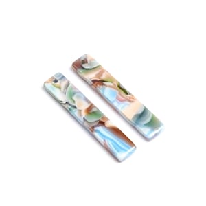 Könnte beinhalten: Zwei lange, rechteckige, marmorierte Acryl-Anhänger mit einem Loch oben. Die Anhänger sind eine Mischung aus Blau, Grün, Braun und Weiß.