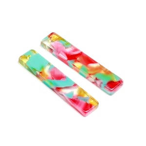 May include: Two long, rectangular, colorful acrylic hair clips. The clips are translucent and have a swirling pattern of pink, green, and yellow.