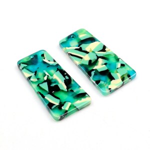 May include: Two rectangular green, blue, and white patterned acrylic resin charms with a hole at the top for hanging.