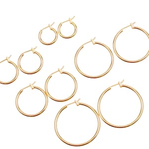 May include: Set of eight gold hoop earrings of varying sizes. The earrings are all simple and circular in shape.