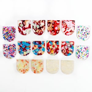 May include: Assortment of 14 colourful, patterned, and glittery resin cabochons in a half-circle shape. The cabochons are perfect for crafting jewellery, hair accessories, and other DIY projects.