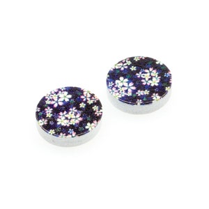 Può includere: Due sottobicchieri rotondi, bianchi, con motivo floreale su sfondo blu scuro. I sottobicchieri hanno un bordo bianco e una base bianca.