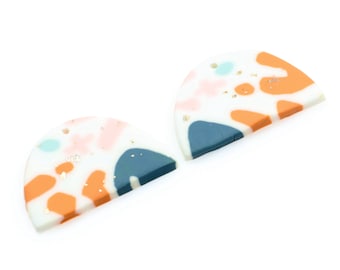 May include: Two half-circle shaped polymer clay earrings with a white base and abstract patterns in shades of orange, pink, blue, and gold glitter.