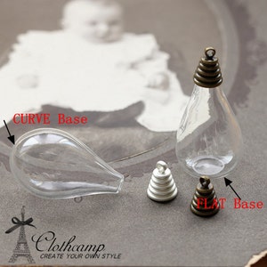Puede incluir: Viales transparentes en forma de lágrima con tapas y bases metálicas. Un vial tiene una base curva, mientras que otro tiene una base plana. También hay dos pequeños amuletos metálicos en capas. La imagen incluye el texto "Clothcamp Create your own style."