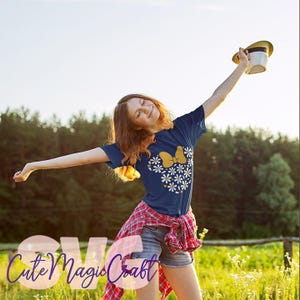 May include: Navy blue t-shirt with a yellow bow and white daisy design. The shirt is part of an SVG design collection. The image shows a person wearing the shirt with a red plaid shirt tied around the waist and holding a hat.