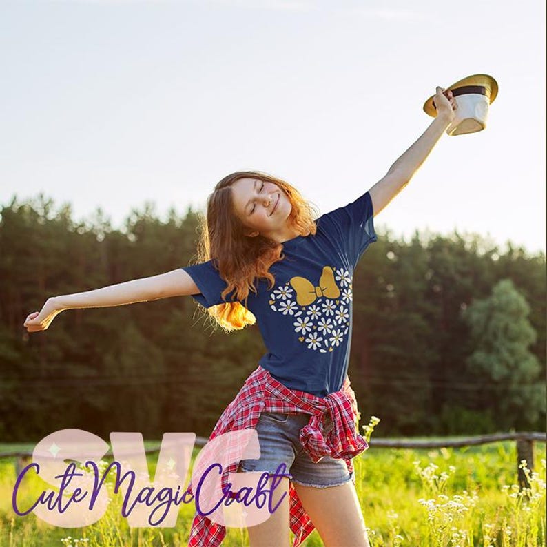 May include: Navy blue t-shirt with a yellow bow and white daisy design. The shirt is part of an SVG design collection. The image shows a person wearing the shirt with a red plaid shirt tied around the waist and holding a hat.