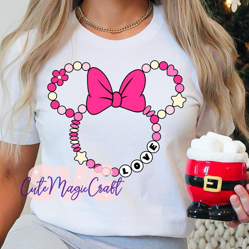 May include: White t-shirt featuring a pink Minnie Mouse design with a bow and the word "LOVE". The design includes pink, yellow, and white beads and stars. A gold necklace is visible. A Santa mug is held in the hand.