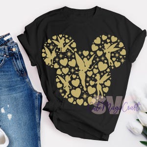 May include: Black t-shirt with a gold design in the shape of Mickey Mouse's head. The design is filled with hearts, stars, and fairy silhouettes. The text "Cute Magi Craft" is visible in the lower right corner.