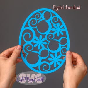 May include: A vibrant blue Easter egg-shaped cut-out design with Mickey Mouse silhouettes and floral patterns. The text "Digital download" is in the upper right. The design is held by two hands.
