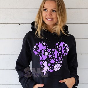 Pu&ograve; includere: Felpa con cappuccio nera con un design a silhouette di Topolino viola riempito di creature marine e bolle. Il design include una sirena, un cavalluccio marino e altri elementi acquatici. La felpa ha una tasca frontale e un cappuccio con coulisse.
