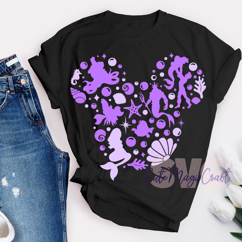 Pu&ograve; includere: T-shirt nera con un design viola a forma di testa di Topolino, riempito di creature marine e bolle. Il design include una silhouette di sirena, stelle marine e cavalluccio marino. Il testo "Cute Magi Craft" &egrave; visibile.