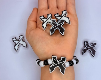 May include: A black and white beaded bracelet with a large X-shaped charm. Several X-shaped charms are scattered around a hand. The charms and bracelet feature a black and white color scheme.
