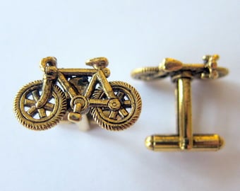 May include: A pair of gold-toned cufflinks featuring a bicycle design. The cufflinks are made of metal and have a polished finish.