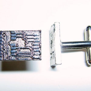 May include: A pair of silver cufflinks with a circuit board design. The cufflinks are made of metal and have a polished finish.