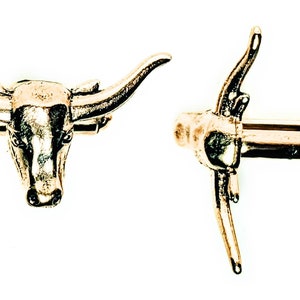 May include: A pair of gold-tone cufflinks. One cufflink features a detailed bull's head design. The other cufflink is a simple, straight design.