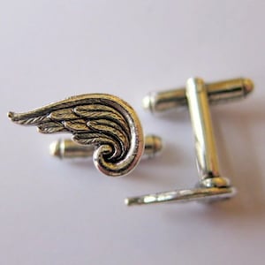 May include: Silver cufflinks with a detailed wing design. The wings are textured and have a 3D effect.