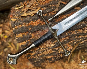 May include: A detailed image of a sword with a silver blade and a black handle. The sword features a crossguard and a pommel with gold accents. The sword is resting on a textured wooden surface.