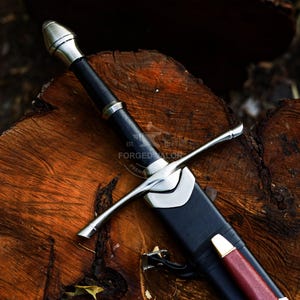 May include: A medieval sword with a black leather-wrapped handle and a silver crossguard. The sword is sheathed in a black scabbard with a red accent. The image includes the text "FORGED VALOR".