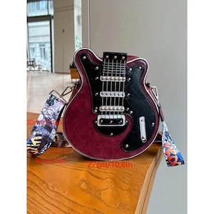 May include: A burgundy and black guitar-shaped handbag with a patterned strap. The bag is approximately 10.6 inches wide and 11.8 inches tall. The strap is 30 cm/11.8 in long. The bag has silver hardware.