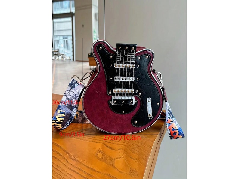 May include: A burgundy and black guitar-shaped handbag with a patterned strap. The bag is approximately 10.6 inches wide and 11.8 inches tall. The strap is 30 cm/11.8 in long. The bag has silver hardware.