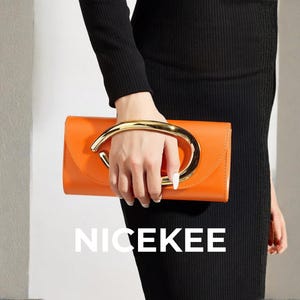 Puede incluir: Bolso de mano naranja con asa dorada. El bolso rectangular tiene un asa curva. La palabra "NICEKEE" está impresa en blanco en la parte inferior de la imagen. El bolso lo sostiene una persona que lleva un vestido negro.
