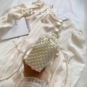 May include: A white beaded handbag with a pearl handle and a long pearl strap. The bag is cylindrical and covered in small, round beads. The word "NICEKEE" is printed in white across the top of the image.