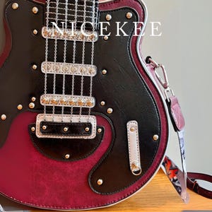 May include: A guitar-shaped handbag in black and burgundy leather with silver-tone hardware. The bag features a shoulder strap and is embellished with decorative studs. The word "NICEKEE" is printed on the top.