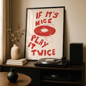 Può includere: Un poster incorniciato con la scritta "IF IT'S NICE PLAY IT TWICE" in rosso, con una grafica di un disco in vinile rosso. Un giradischi nero è su un mobile in legno scuro, con un altoparlante nero e un vaso decorativo.