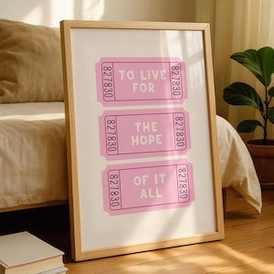May include: A framed print with a light wood frame. The print features three pink ticket-shaped designs with the words "TO LIVE FOR", "THE HOPE", and "OF IT ALL" in white text. The background is a soft cream color.