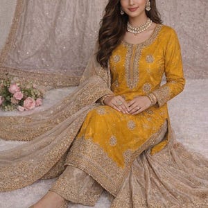 Könnte beinhalten: Senfgelbes, goldbesticktes Salwar Kameez mit passendem Dupatta. Das Outfit weist aufwendige Goldstickereien am Ausschnitt, an den Ärmeln und am Saum auf. Das Ensemble umfasst eine passende, goldverzierte Hose und goldene Ballerinas. Der Hintergrund ist neutral.